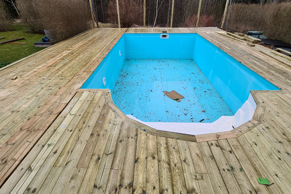 Pool under byggnation, omgiven av nylagt trädäck i ljust trä.